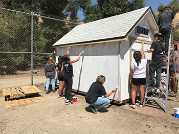 group of students and adults painting shed white